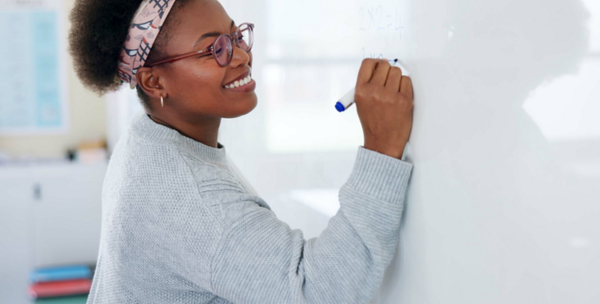 A smiling woman writes on a whiteboard.